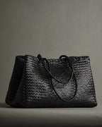ALEO Romy Woven Tote in Black with braided handles on a grey studio backdrop