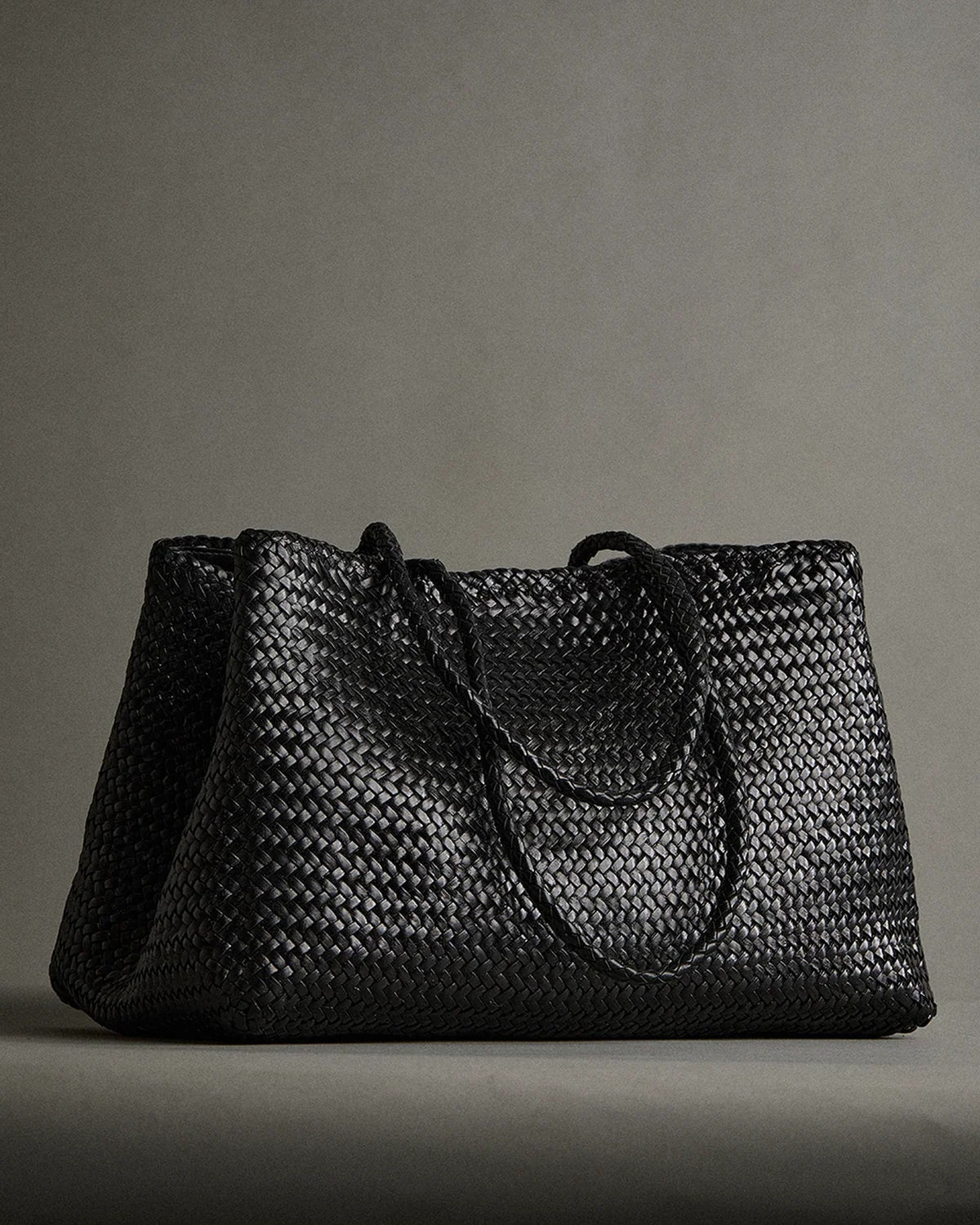 ALEO Romy Woven Tote in Black with braided handles on a grey studio backdrop