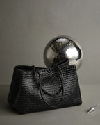 ALEO Romy Woven Tote in Black styled with a silver sphere on a grey studio backdrop