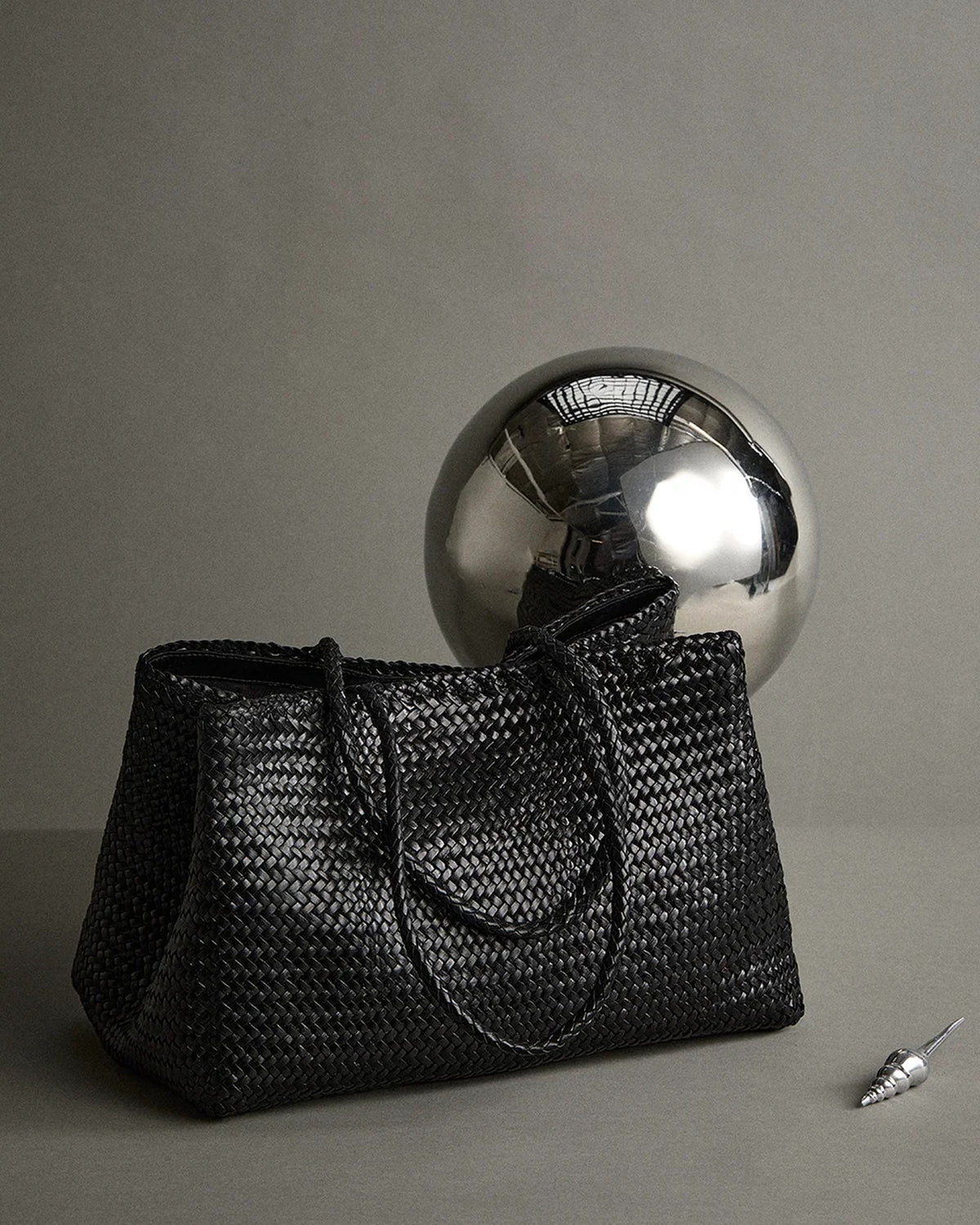 ALEO Romy Woven Tote in Black styled with a silver sphere on a grey studio backdrop