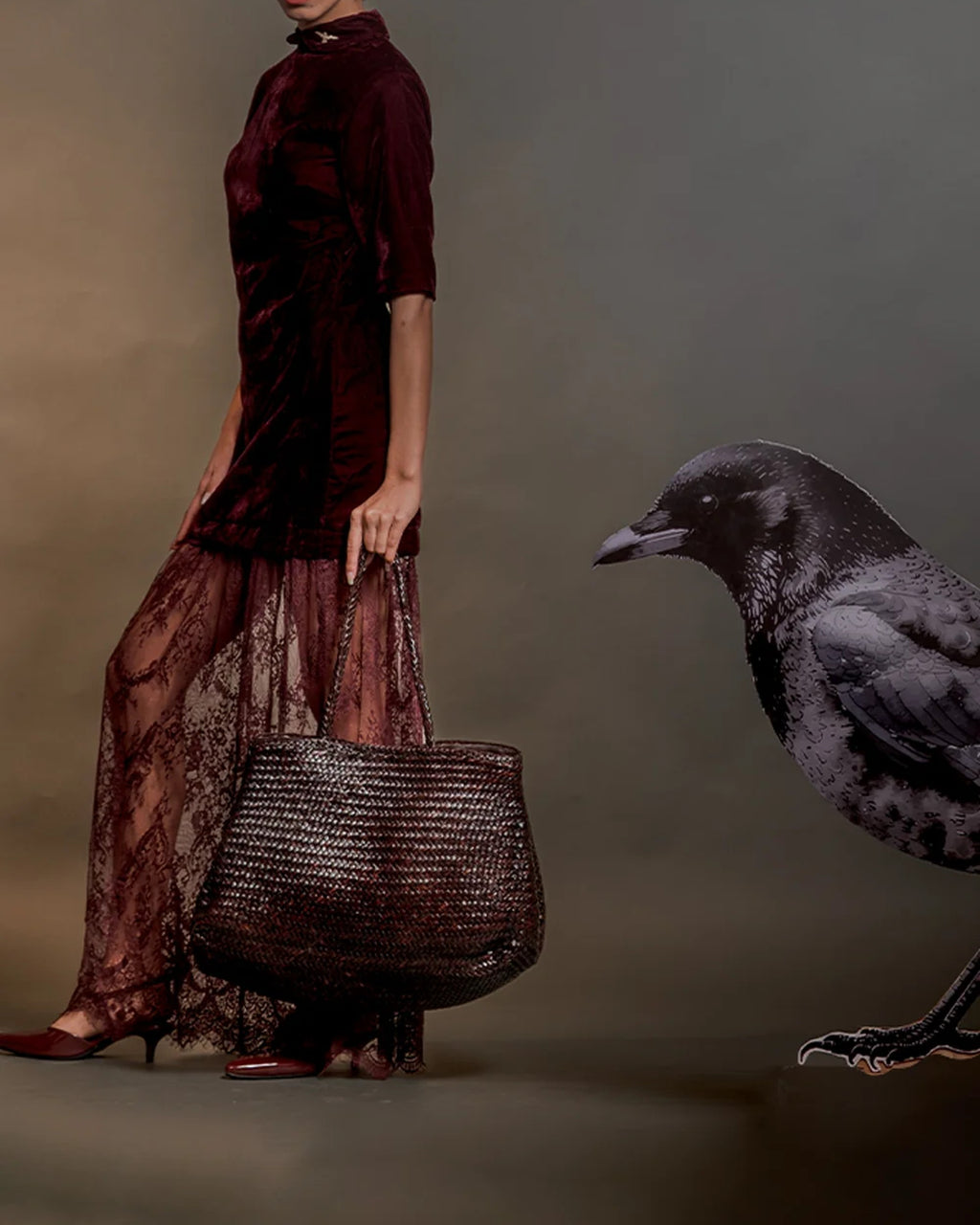 Model carrying the ALEO Romy Woven Tote in Crema by its braided handles, with a black crow beside her
