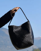 ALEO Toka Woven Tote in Black held by its woven strap against a clear blue sky