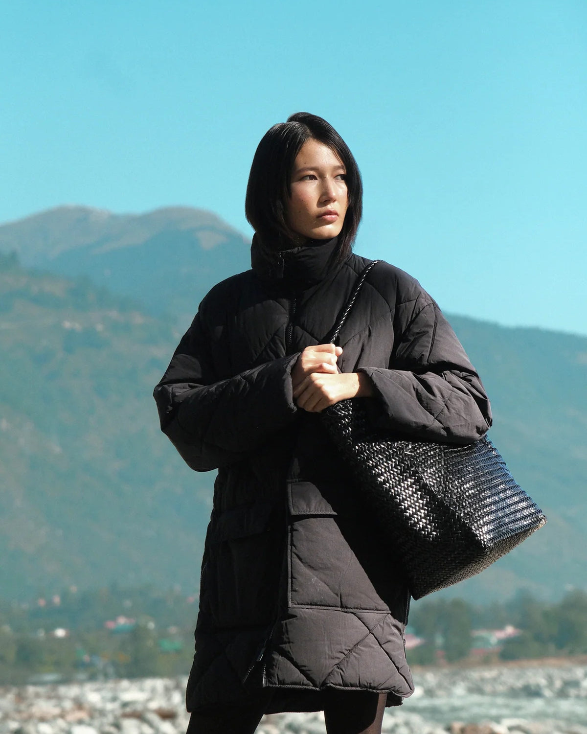 Model wearing the ALEO Toka Woven Tote in Black on her shoulder against a blue sky