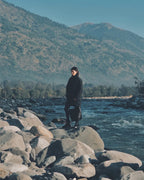 Model standing on rocks by a river holding the ALEO Toka Woven Tote in Black