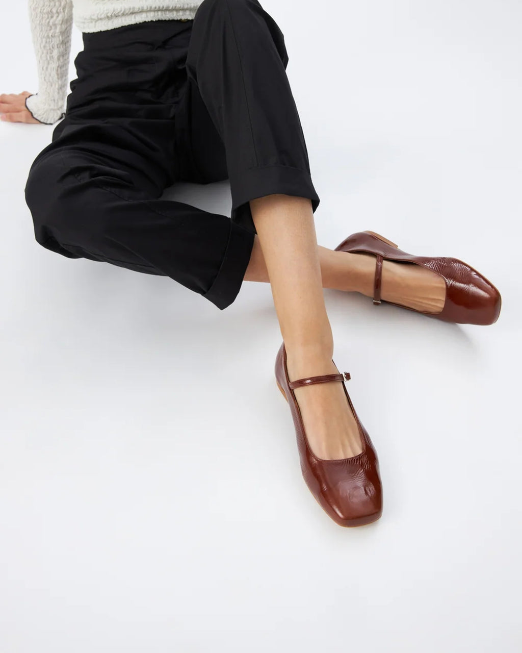 Model seated with crossed legs wearing Augusta saddle patent leather Mary Jane flats
