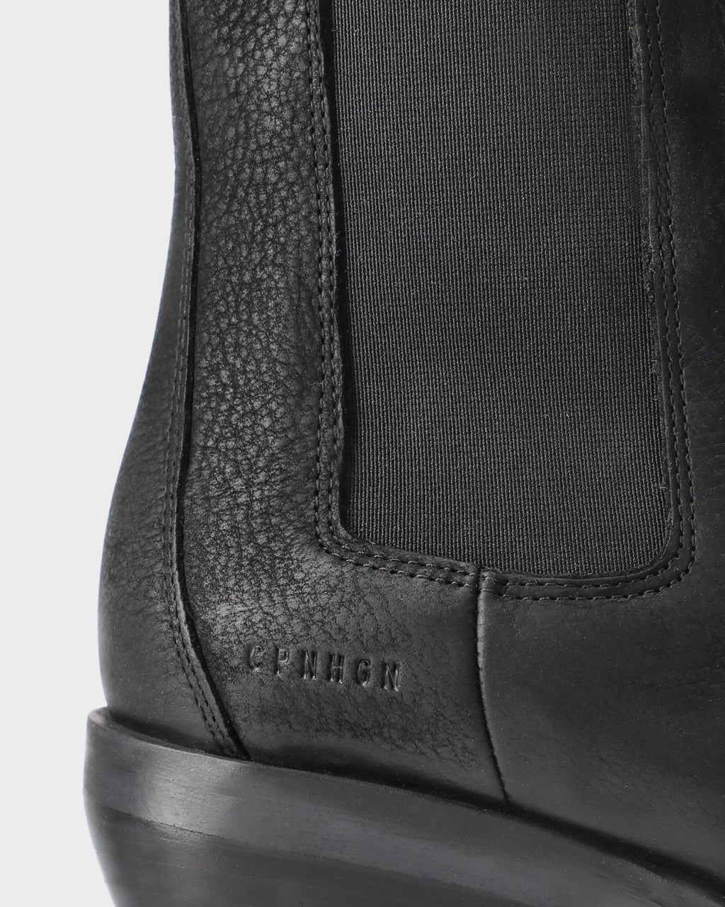 Close-up of the embossed logo and elastic side panel on a black waxed nubuck Chelsea boot