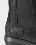 Close-up of the embossed logo and elastic side panel on a black waxed nubuck Chelsea boot