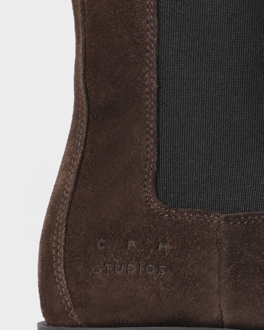 Close-up of the Copenhagen Studios logo and stitching on chocolate brown suede