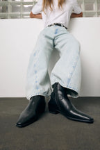 Model wearing Copenhagen Studios black leather ankle boots with light wash wide-leg jeans