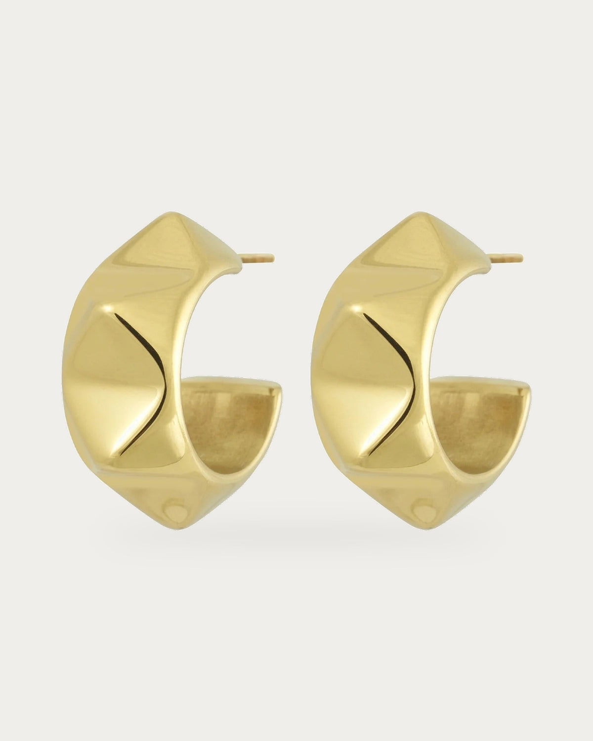 Edblad Peak Rivet Creole Earrings In Gold, a pair of wide gold creole earrings with soft square rivets, product photo on a soft off-white background