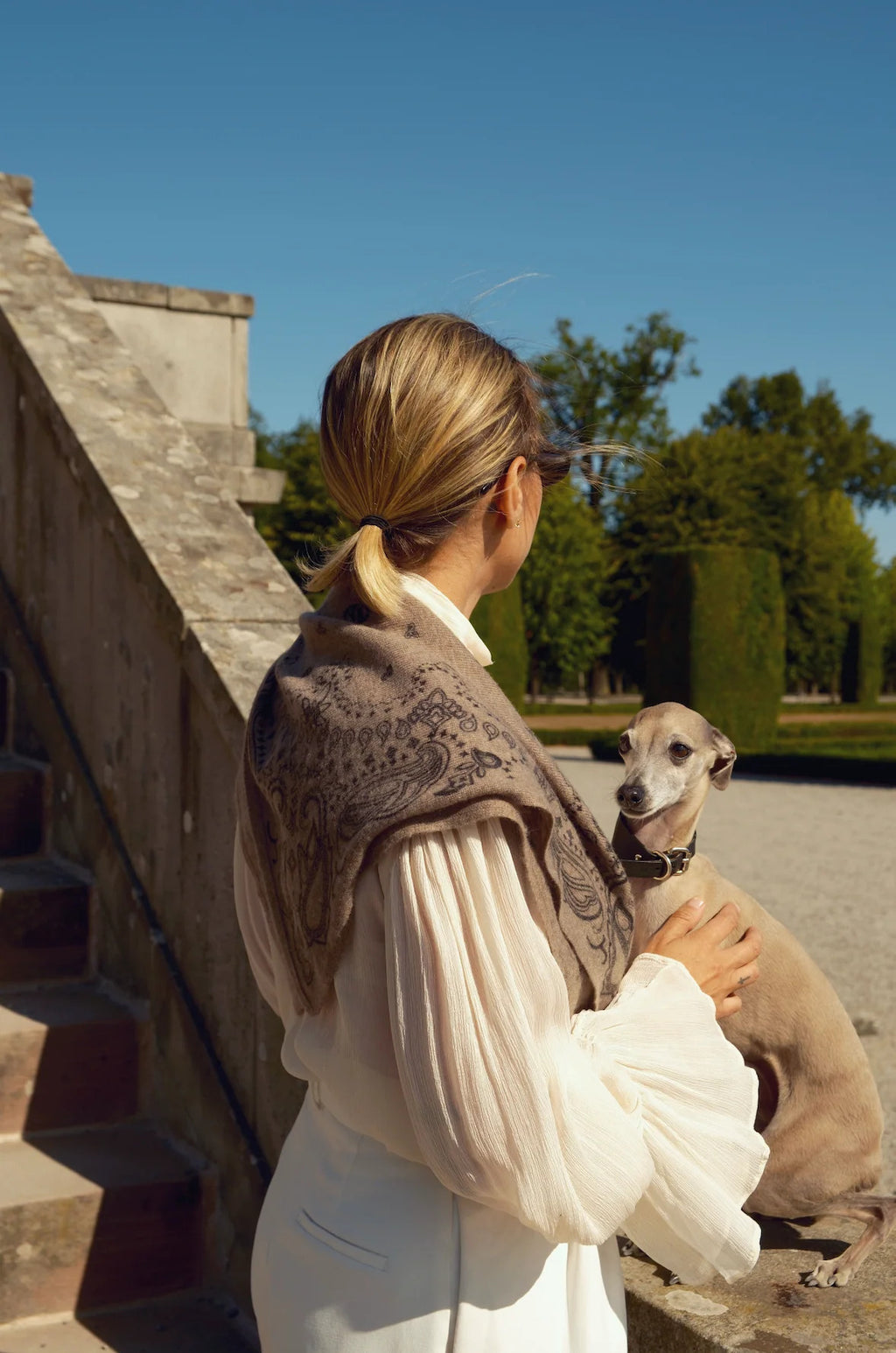 Lescarf cashmere paisley scarf in greige worn over the shoulders with a white blouse