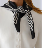 Lescarf cashmere striped scarf in black and cream, knotted at the neck with a white jacket