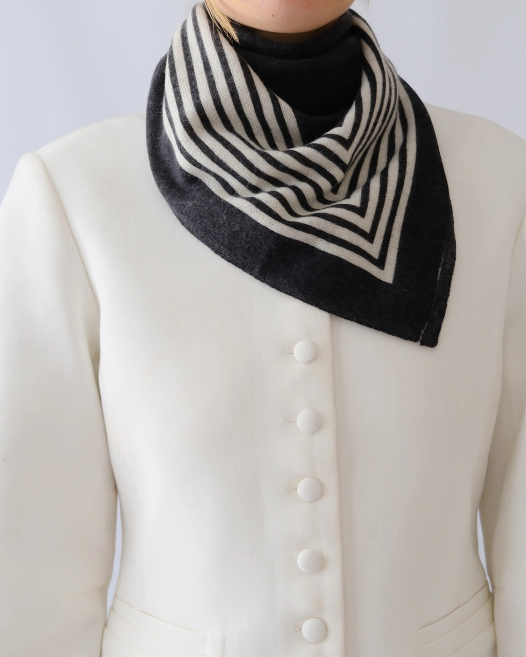 Lescarf cashmere striped scarf in black and cream, worn folded at the neck with a white jacket