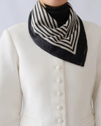 Lescarf cashmere striped scarf in black and cream, worn folded at the neck with a white jacket