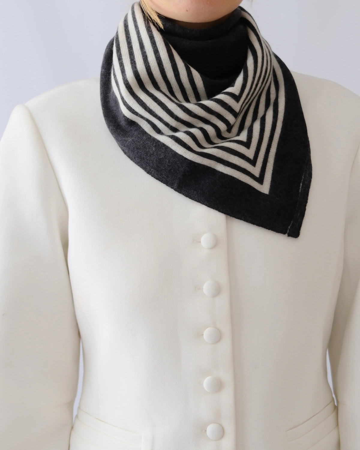 Lescarf cashmere striped scarf in black and cream, worn folded at the neck with a white jacket