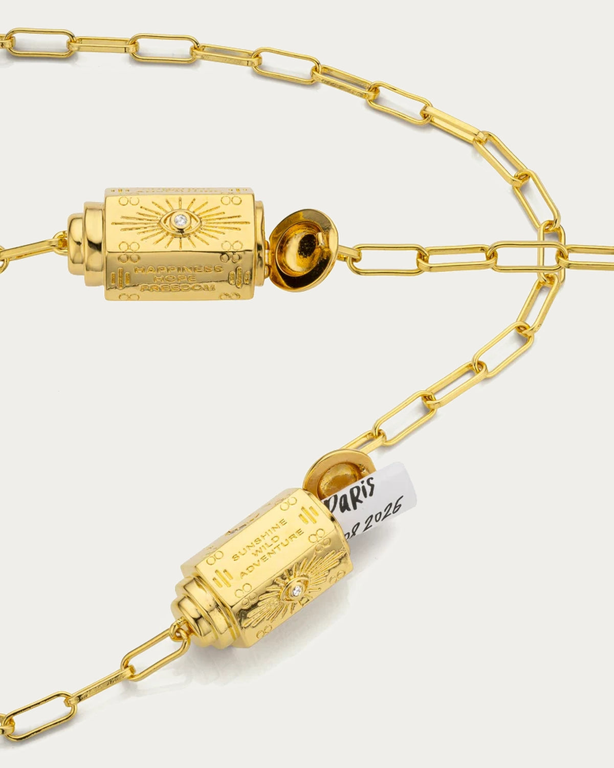 Two MYA—BAY Martinique barrel pendants with the lids open, engraved with eye motifs and short messages
