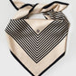 No.1 in Sand scarf by Lescarf folded and knotted, laid flat to show the black striped pattern on sand