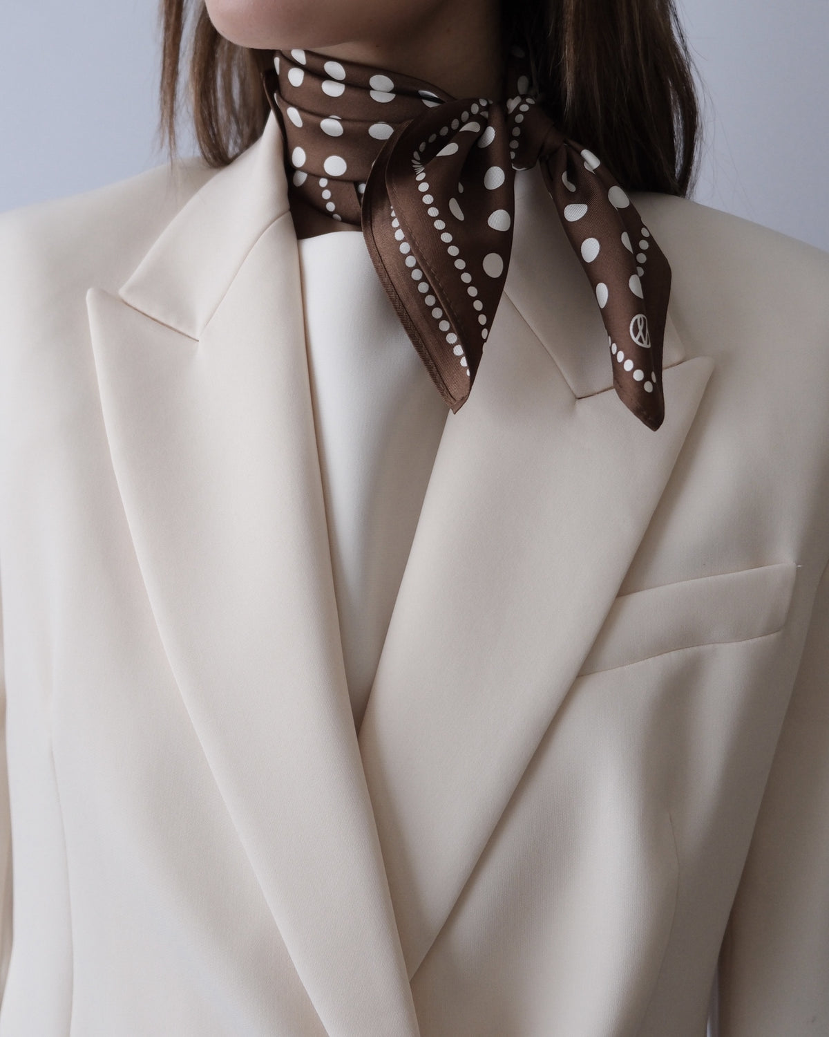 Polkadot Scarf in Brown by Lescarf knotted at the neck and worn with a cream blazer