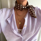 Polkadot Scarf in Brown by Lescarf knotted at the neck over a lilac cardigan with gold necklaces