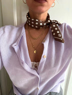 Polkadot Scarf in Brown by Lescarf knotted at the neck over a lilac cardigan with gold necklaces