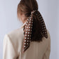 Polkadot Scarf in Brown by Lescarf tied around a ponytail, seen from the back with a cream blazer