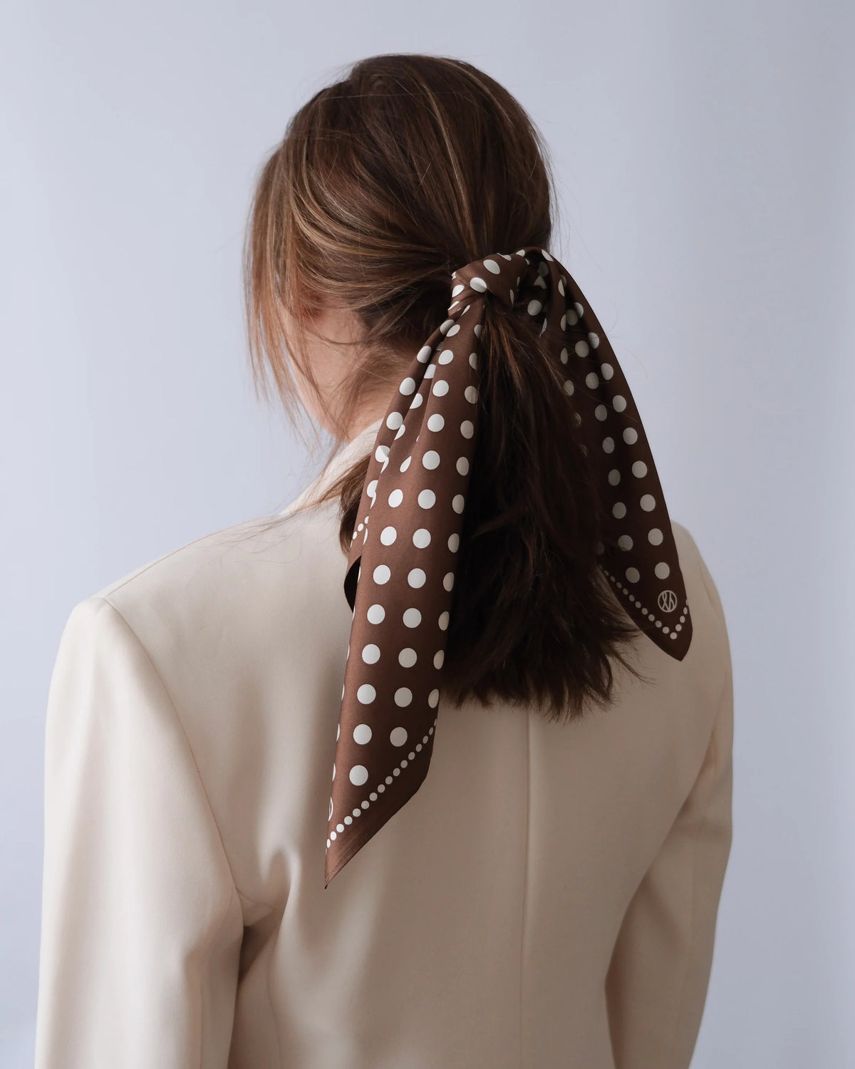 Polkadot Scarf in Brown by Lescarf tied around a ponytail, seen from the back with a cream blazer